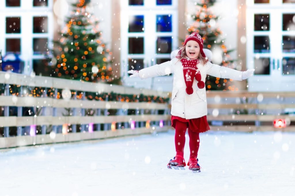 Young girl ice skating with Christmas tree in background - Couple unwraps red Christmas present with large bow - Unwrap the Gift of Travel - Best Western & AAA Travel